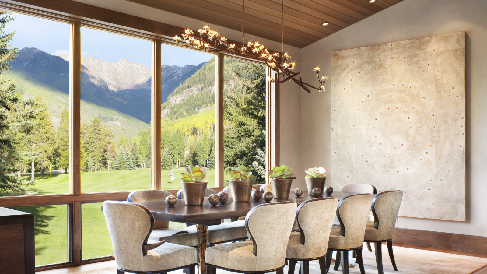 Dining area with neutral artwork, organic chandelier, floor to celling windows, and views of the golf course and mountains.
