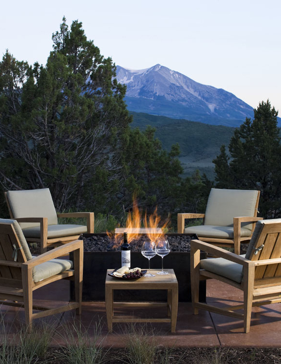 outdoor fire pit surrounded by teak chairs and a mountain backdrop
